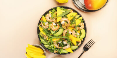 Seafood salad with mango shrimps avocado walnut spinach arugula top view pink background